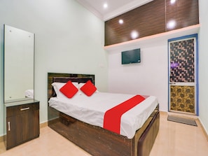 A bedroom with a bed, a nightstand, a mirror, a wall-mounted TV, and a patterned door. - Hotel O Kanha (Nagpur)
