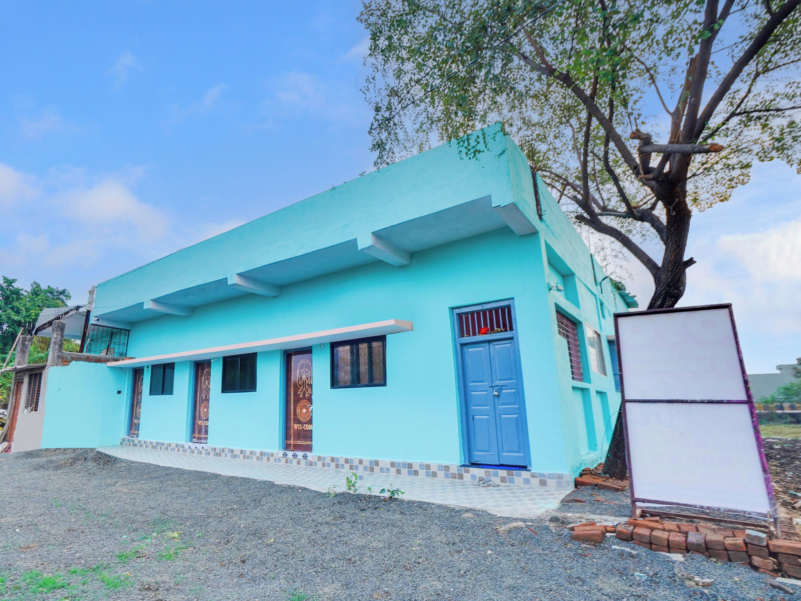 A single-story building with a blue door and windows, a small porch area, and a tree in front.