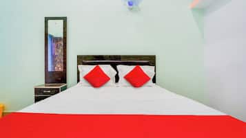 Quarto de hotel com cama, mesa de cabeceira, espelho e ventoinha fixada na parede.