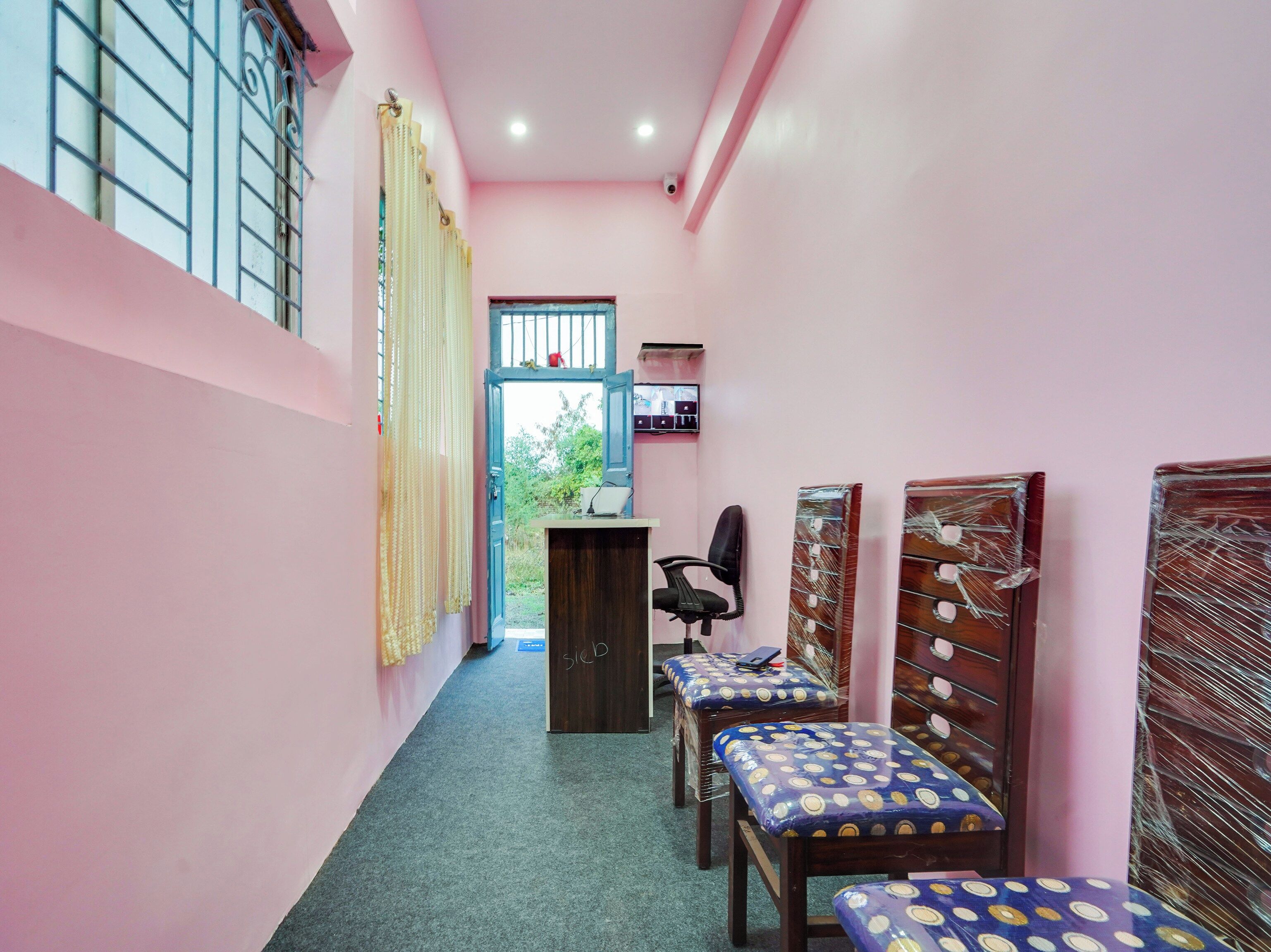 A hallway with pink walls, a desk with a computer, and two chairs with patterned cushions.