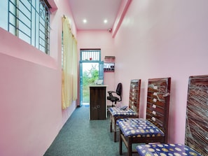 A hallway with pink walls, a desk with a computer, and two chairs with patterned cushions. - Hotel O Kanha (Nagpur)