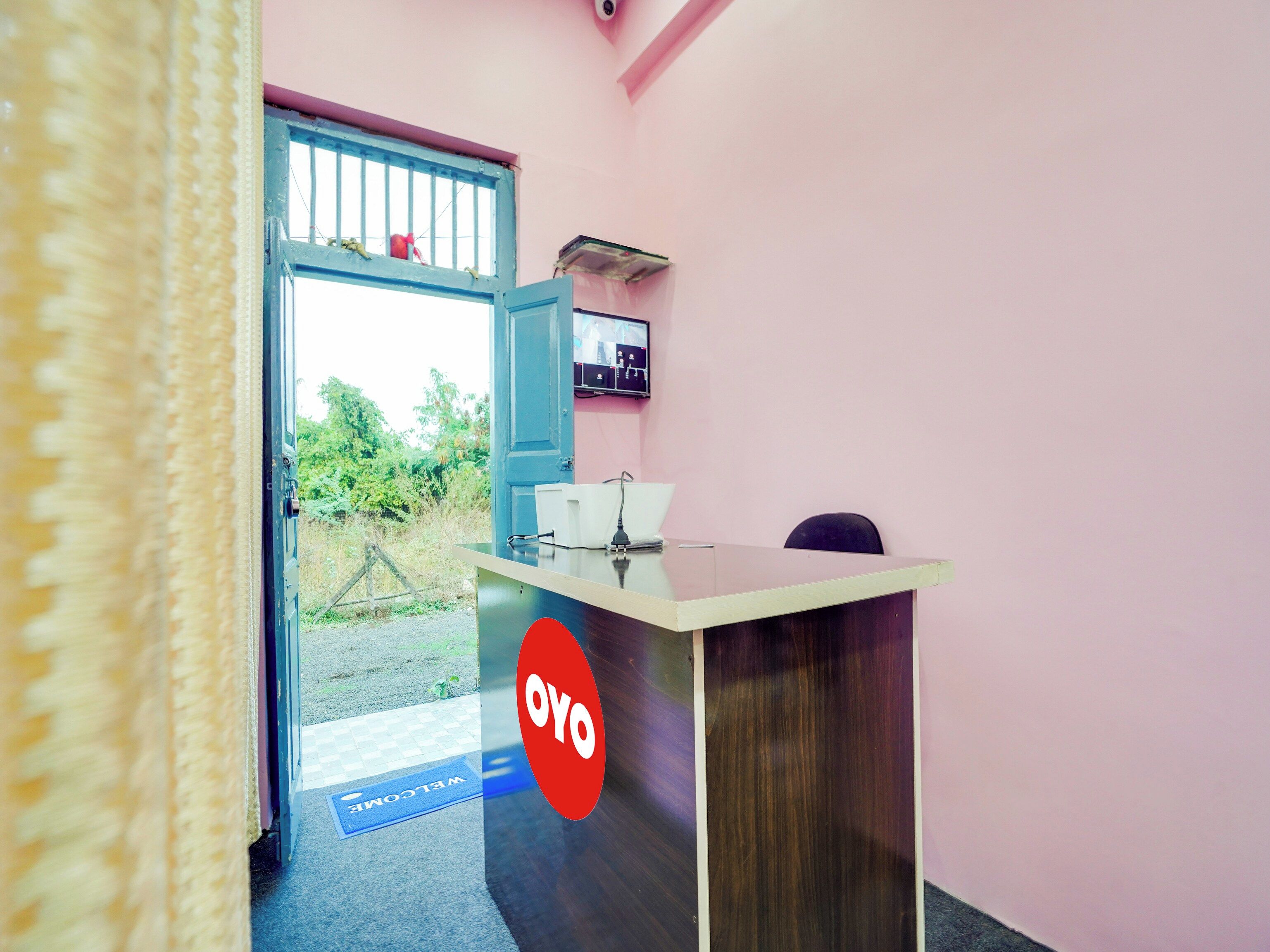 Un mostrador de recepción con un tapete de 'Welcome', una puerta azul y un televisor montado en la pared.