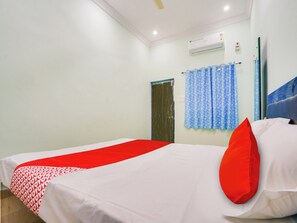 Quarto de hotel com uma cama, um travesseiro vermelho, cortina azul e unidade de ar condicionado.