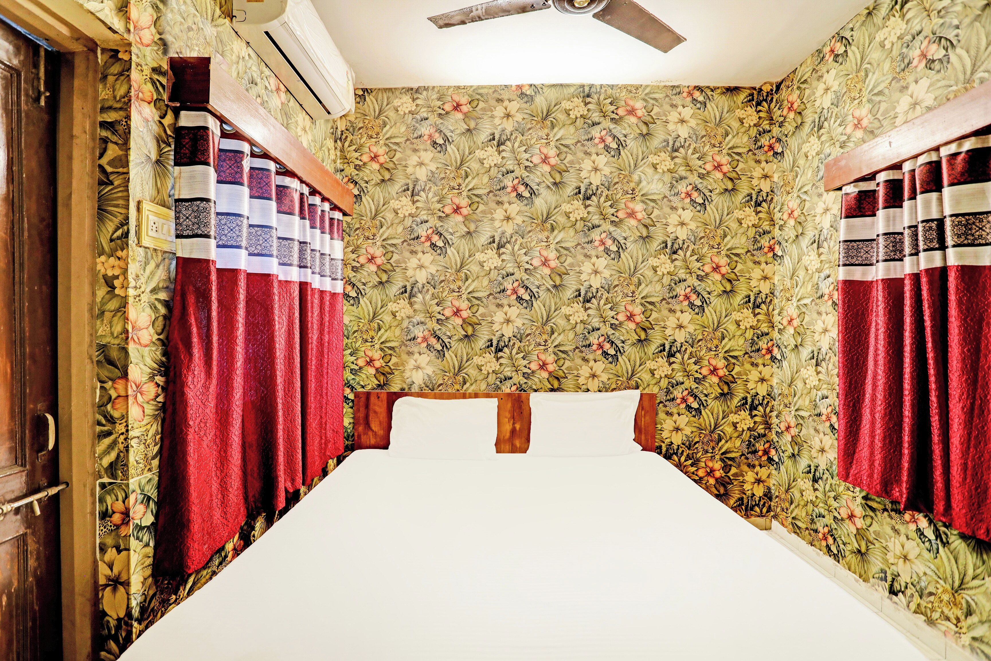 Una habitació amb un llit, paper pintat floral i cortines.