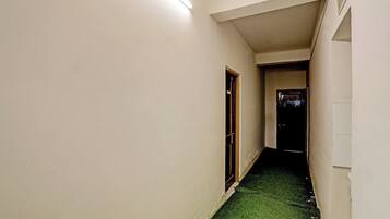 A narrow hallway with a green carpet, white walls, and a door at the end.
