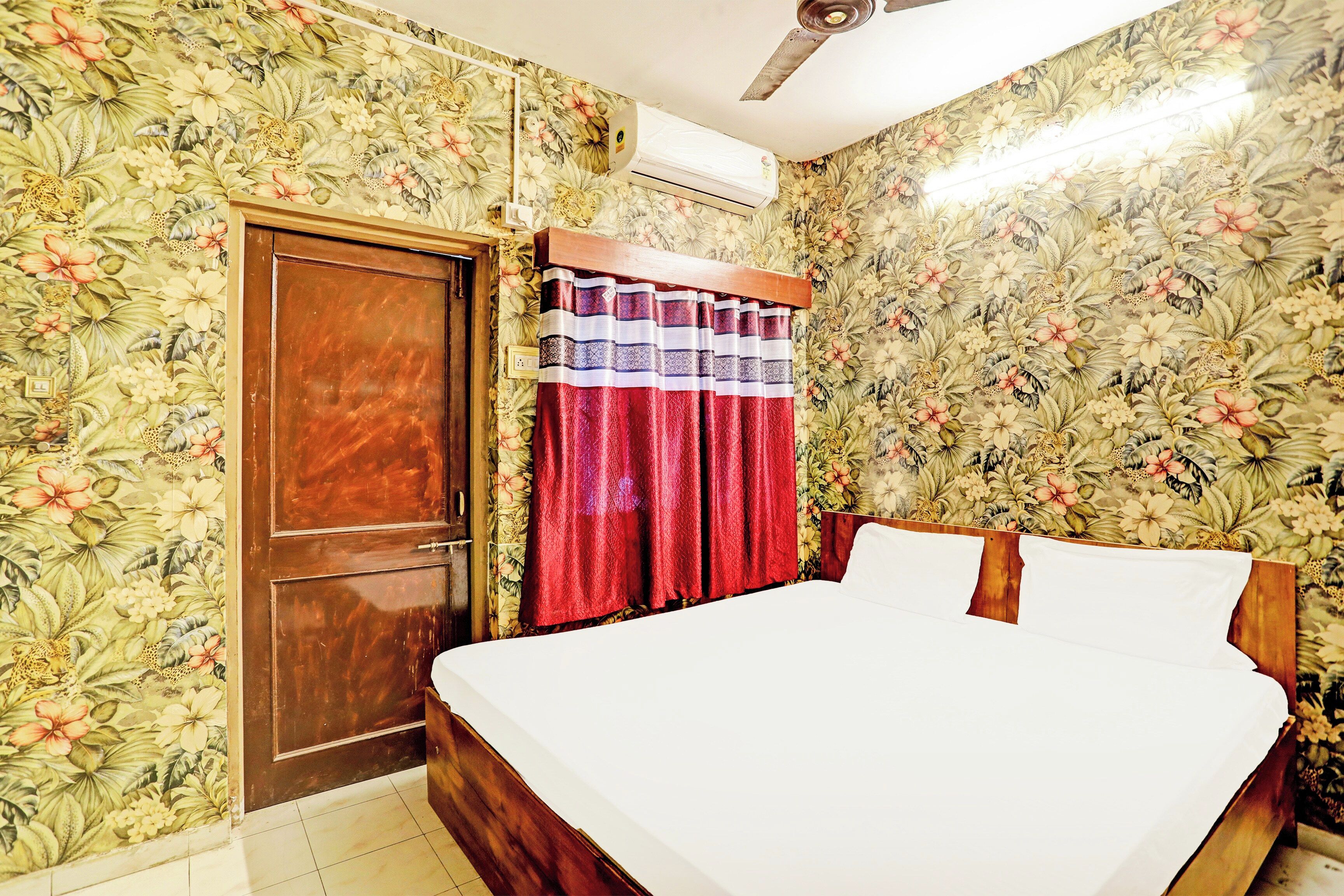 A bedroom with floral wallpaper, a wooden door, a bed with white linens, and a ceiling fan.