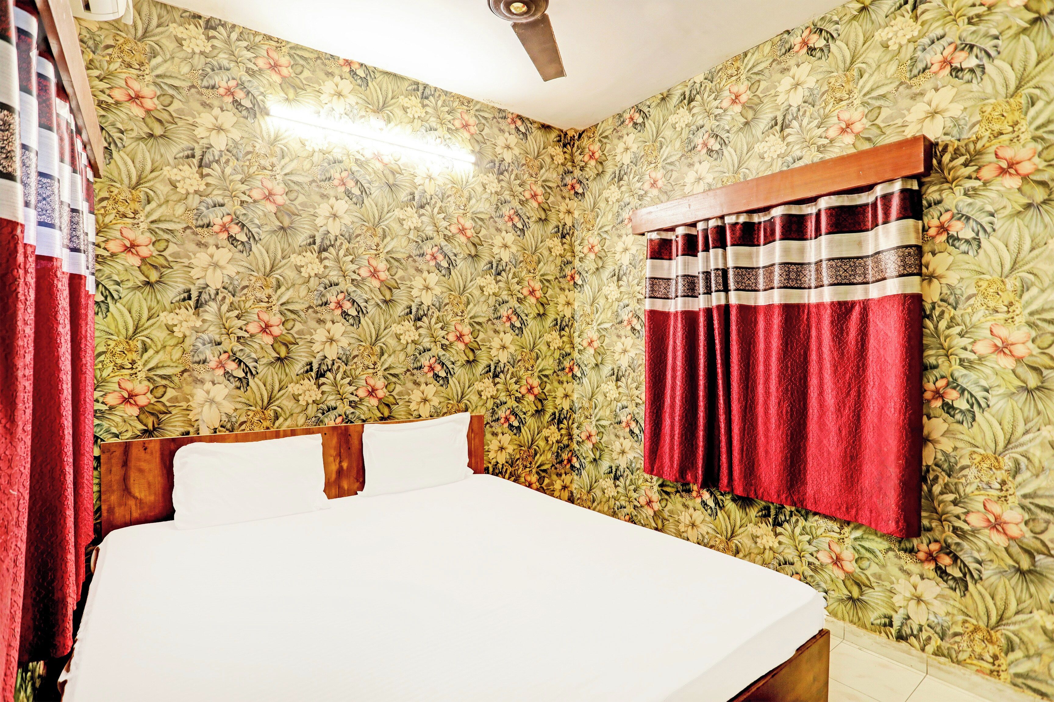 A room with floral wallpaper, a bed with white linens, and a red curtain.