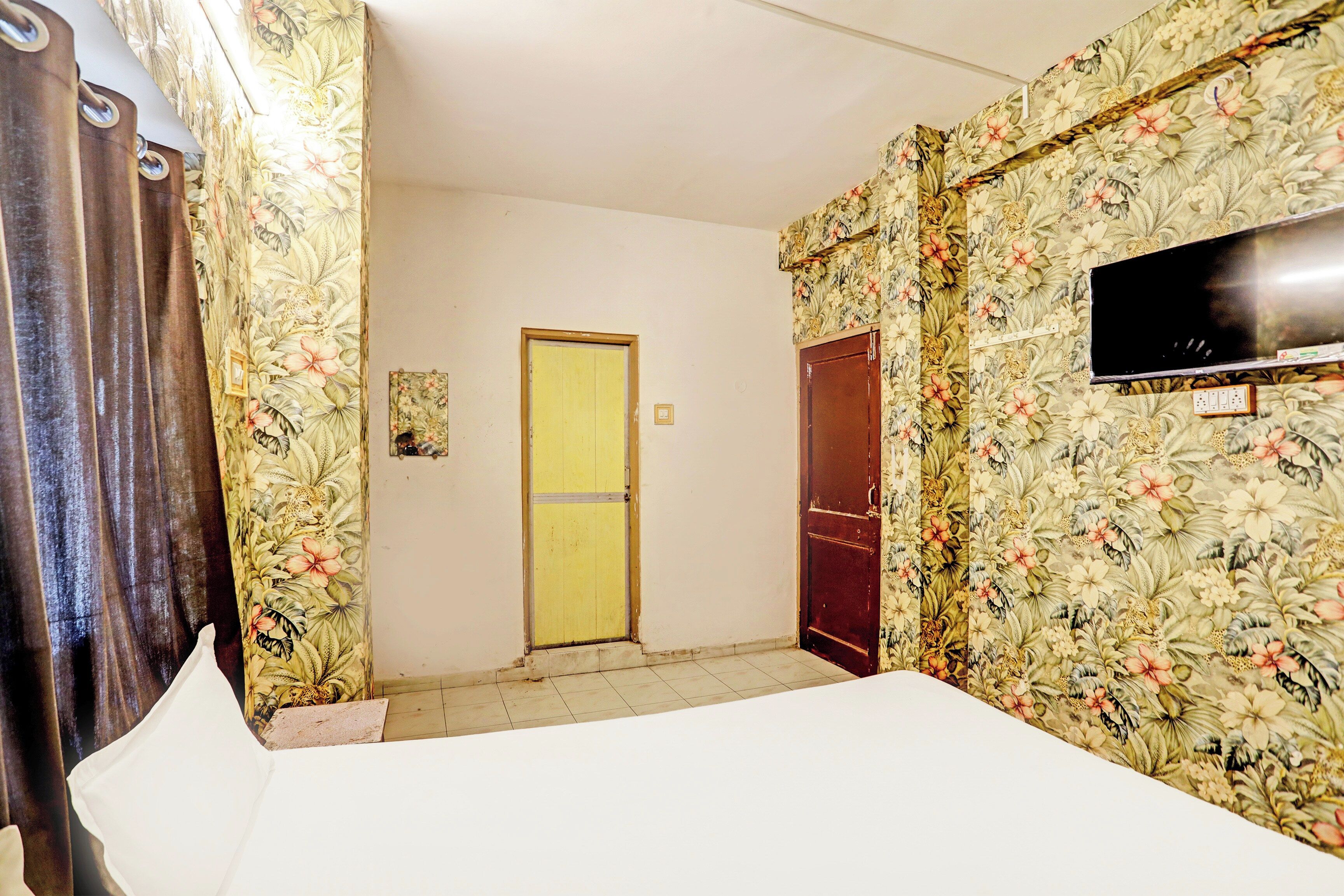 Habitación de hotel con cama, televisor montado en la pared y papel tapiz floral.