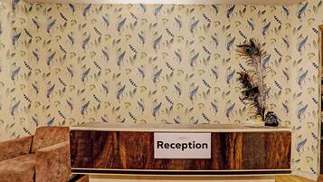 A reception desk with a 'Reception' sign, a brown upholstered armchair, and a patterned wallpaper with leaf and feather designs.