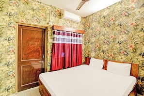 A bedroom with a wooden door, a bed with white bedding, a red curtain, and floral wallpaper. - Hotel O Marina Hotel (Nagpur)