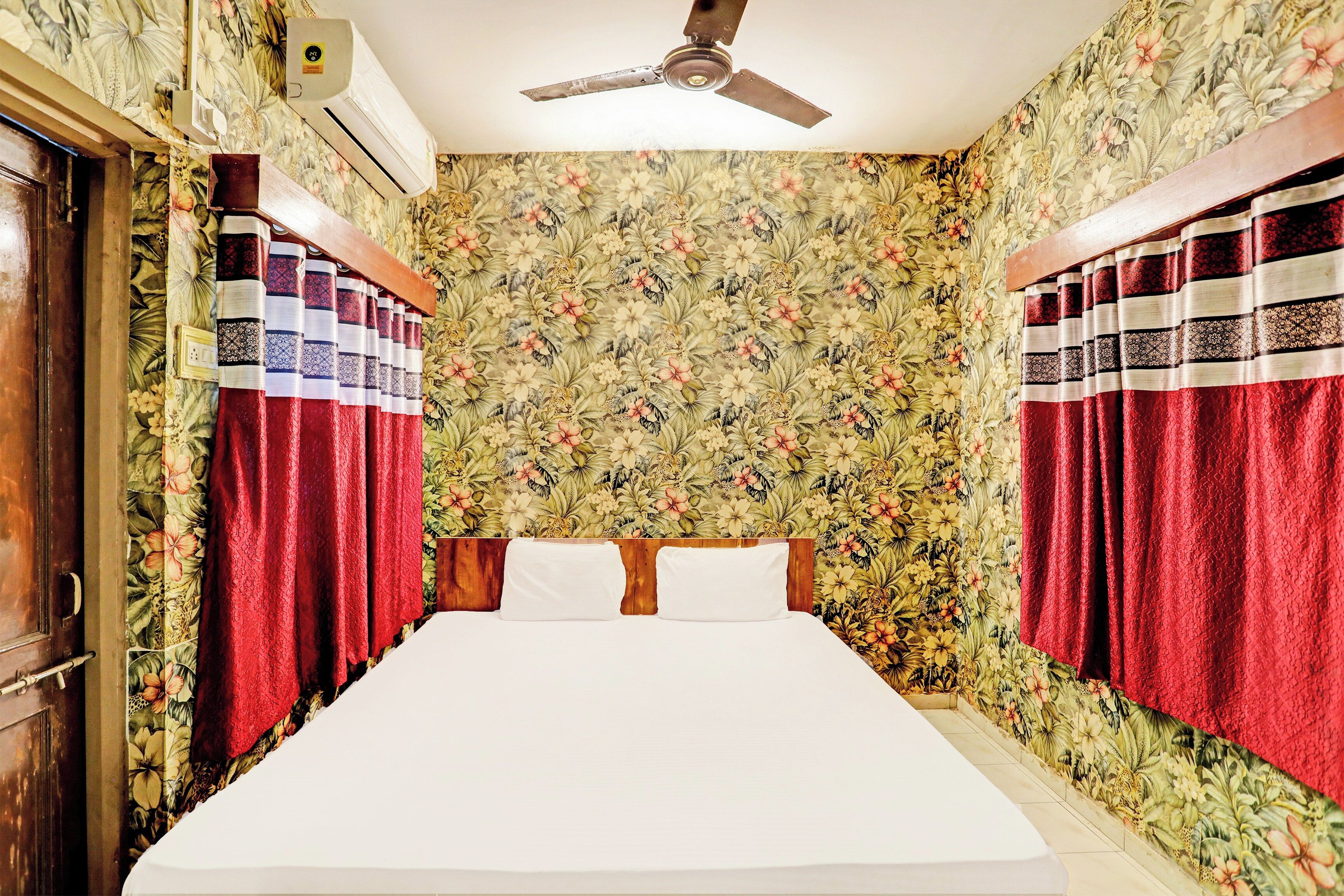 A bedroom with a bed, curtains, a ceiling fan, and floral wallpaper.