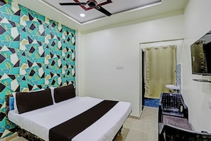 A hotel room with a bed, a ceiling fan, a bathroom with a shower curtain, and a TV mounted on the wall. - Hotel O by OYO P S (Nagpur)
