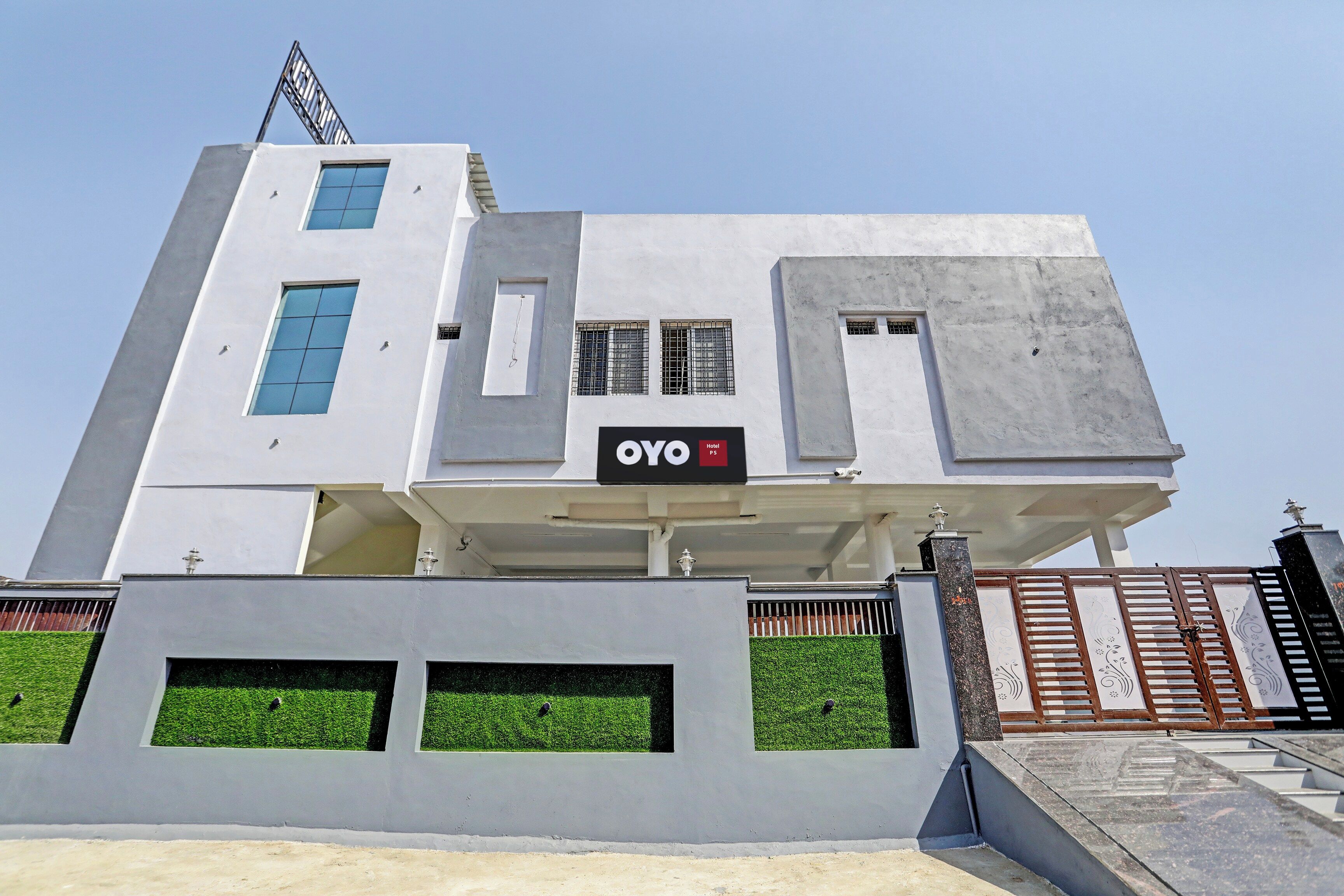 A modern hotel building with a prominent 'OYO' sign, multiple windows, and a gated entrance.
