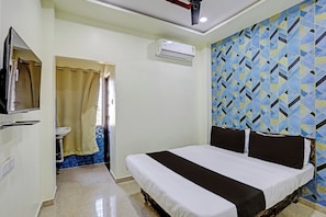 A hotel room with a bed, a TV, an air conditioner, and a bathroom with a shower curtain. - Hotel O by OYO P S (Nagpur)