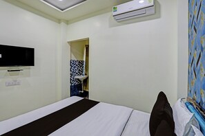 Habitación de hotel con cama, televisión montada en la pared, equipo de aire acondicionado y baño visible a través de una puerta abierta.