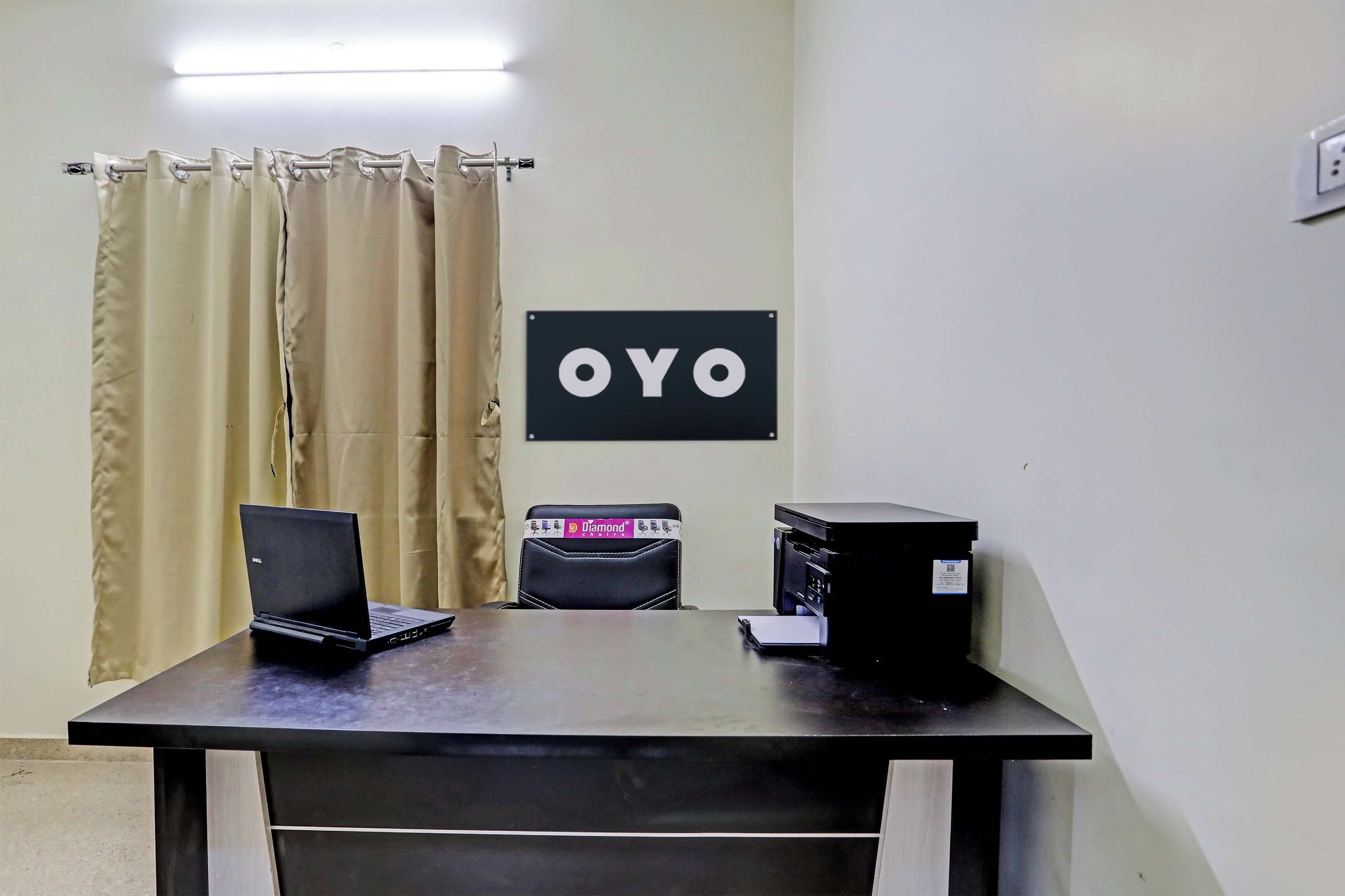 Una habitación con escritorio, dos computadoras portátiles, una impresora y un cartel con 'OYO' en la pared.