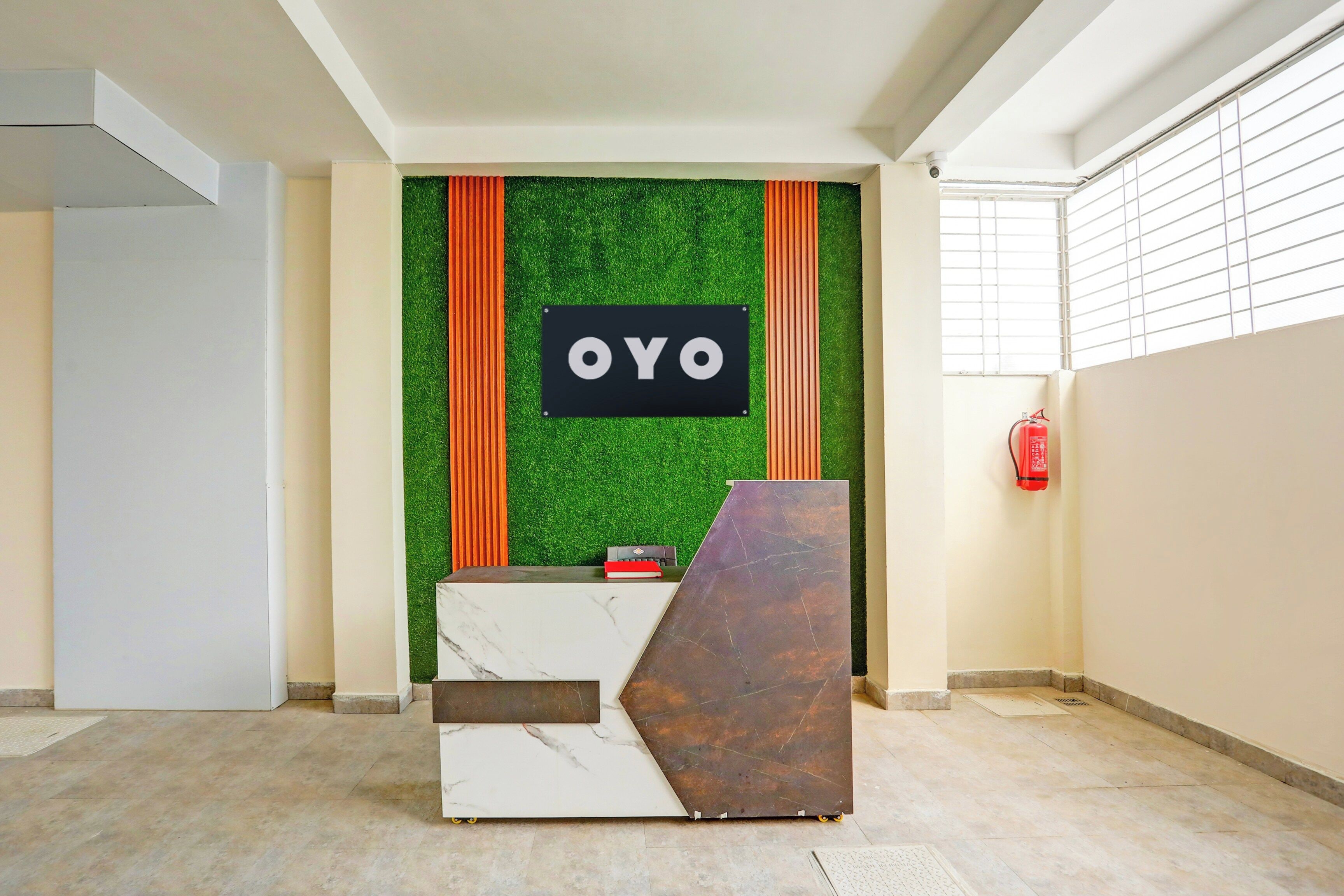 Un comptoir d’accueil avec une enseigne indiquant « OYO », le tout placé devant un mur vert orné de rayures orange verticales.