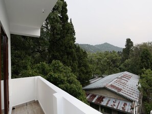 A building with a rusted metal roof, surrounded by dense green trees and a mountain in the background. - Hotel O Summer King (Nainital)