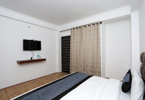 Habitación de hotel con cama, televisor de pantalla plana en la pared, piso de madera y cortina en la ventana.