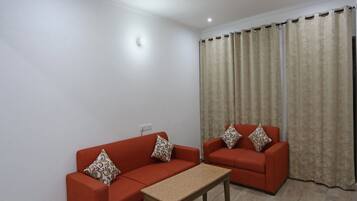 Una sala de estar con dos sofás rojos, una mesa de centro de madera y cortinas color crema.