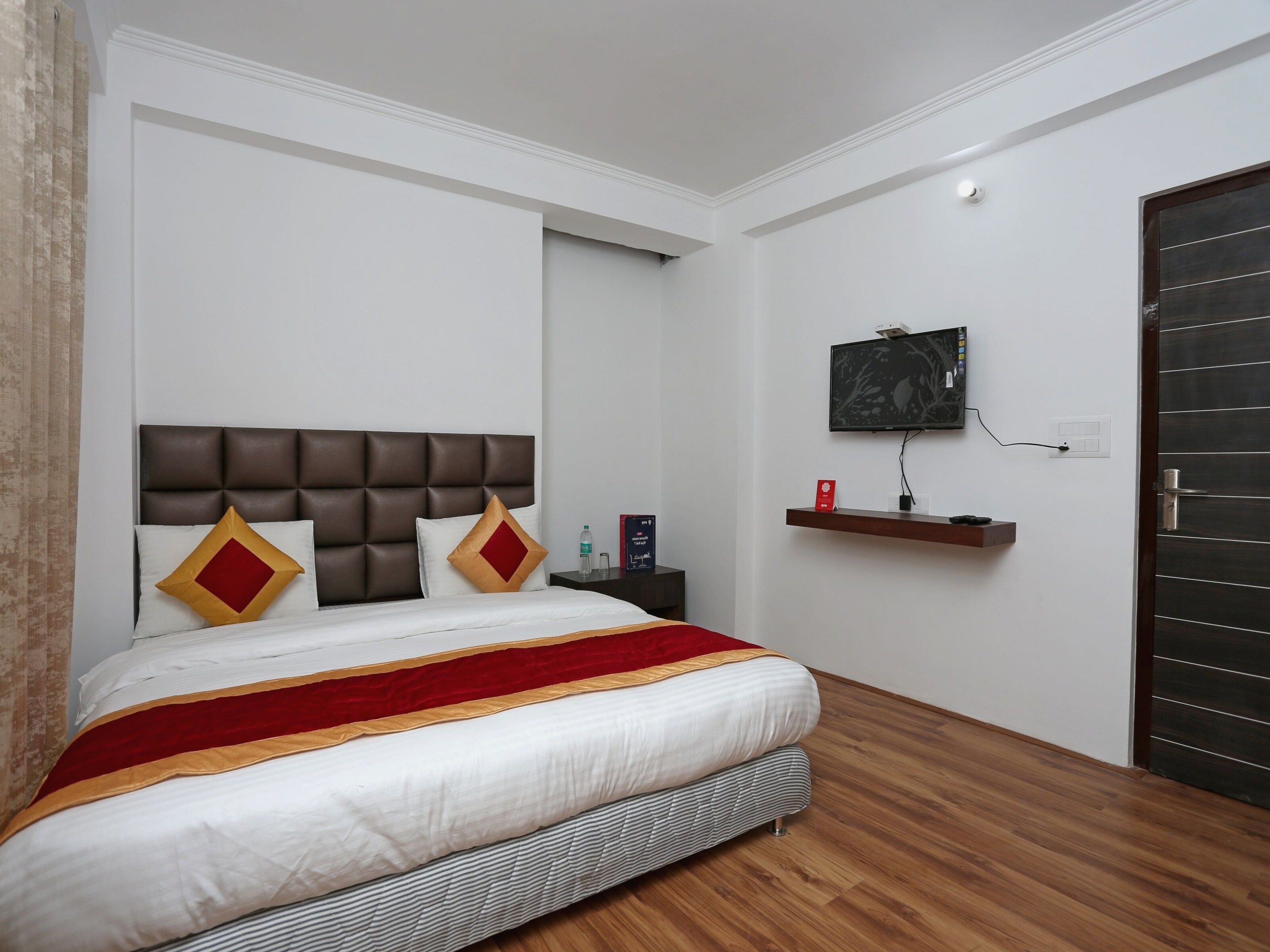 A hotel room with a bed, a television mounted on the wall, and a wooden floor.