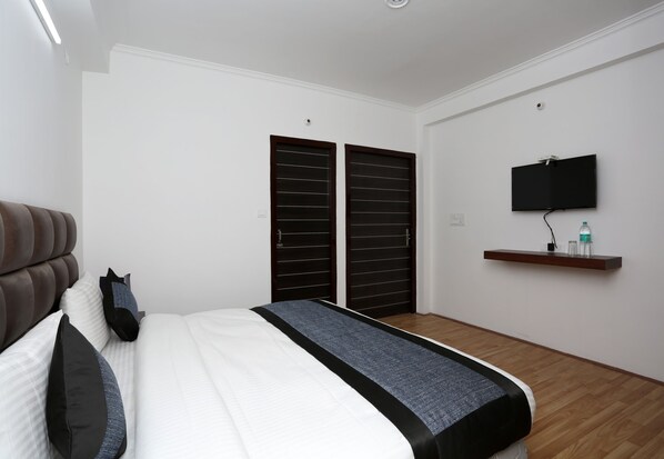 A bedroom with a bed, a TV mounted on the wall, and a wooden floor. - Hotel O Summer King (Nainital)