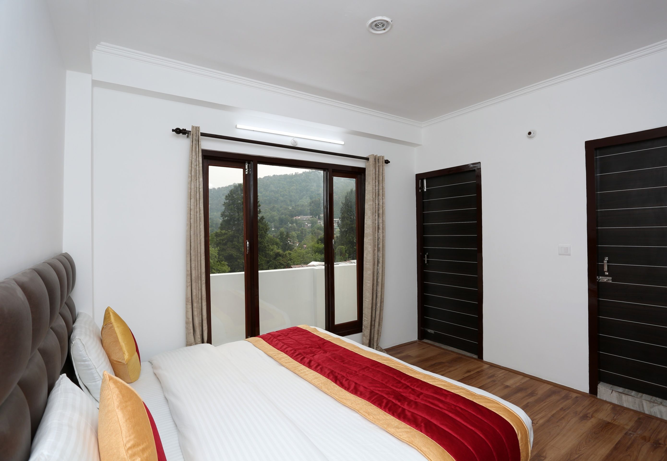 Un dormitorio con cama, ventana con cortinas, puerta y vista a un  área boscosa.