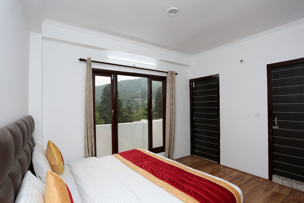 Un dormitorio con cama, ventana con cortinas, puerta y vista a un área boscosa.