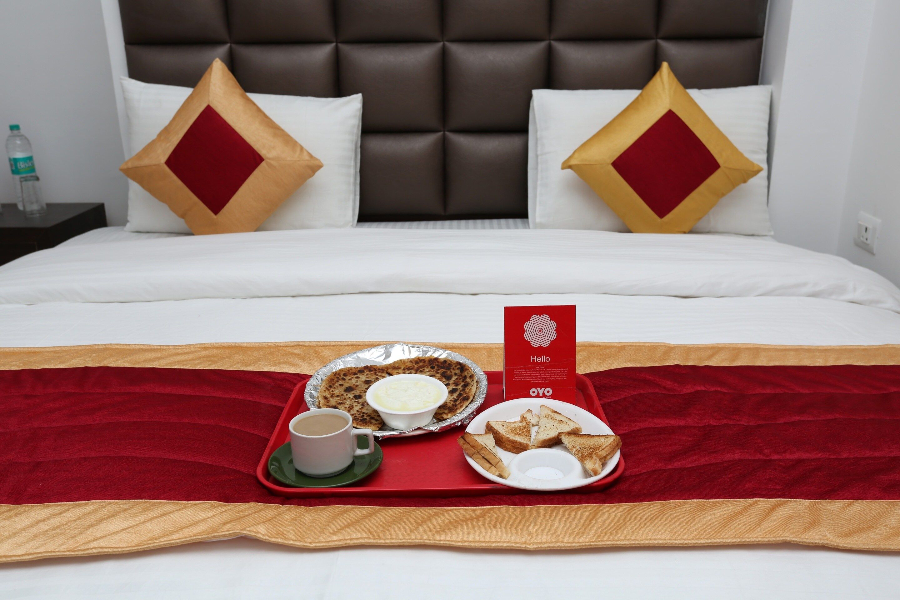 Una habitación de hotel con una cama, una bandeja roja con provisiones de desayuno y un letrero rojo.