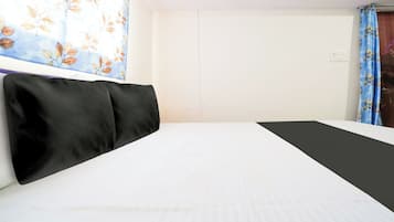 Quarto de hotel com cama, janela com cortina florida e parede lisa.