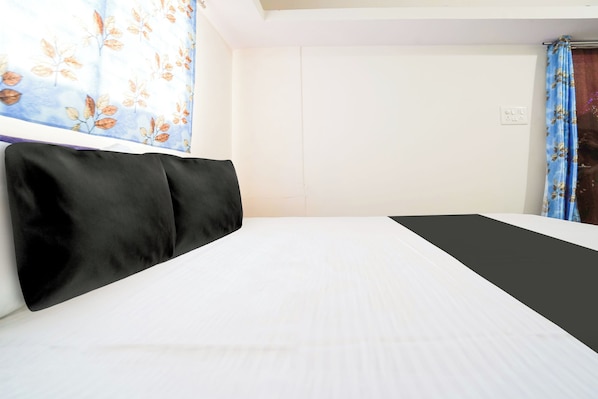 A hotel room with a bed, a window with a floral curtain, and a plain wall. - Hotel O Crown (Nagpur)
