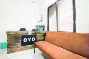 A reception area with a wooden desk labeled 'OYO,' a sofa, a trash bin, and a window with blinds. - Hotel O Crown (Nagpur)