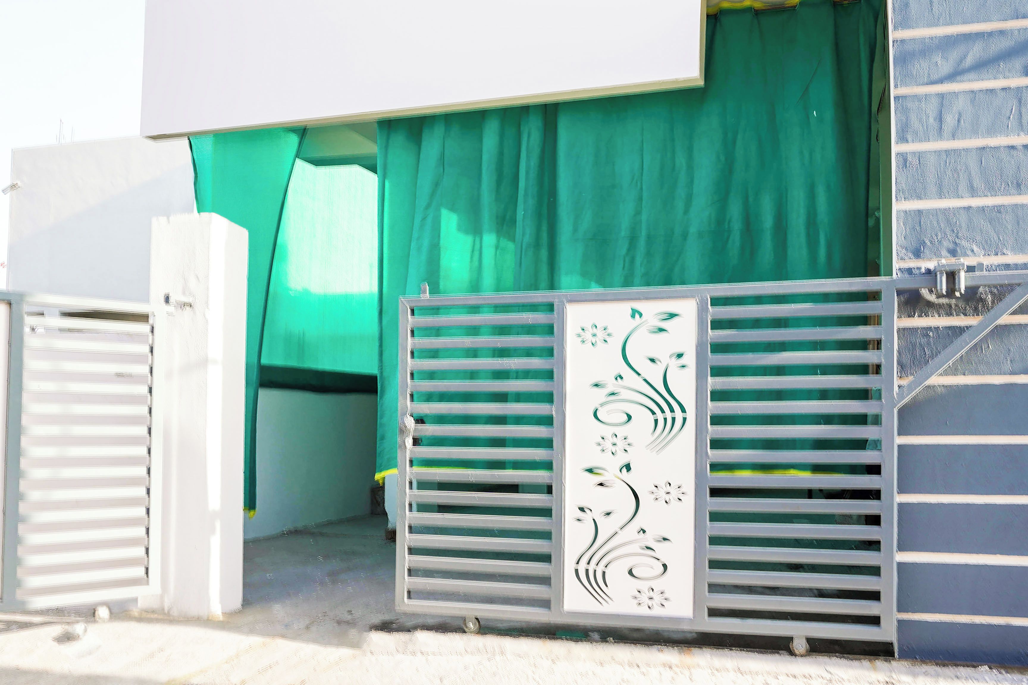 Uma entrada fechada por portão de metal decorativo e uma cortina verde cobrindo parcialmente a porta.