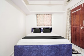 A bedroom with a bed, a window with a patterned curtain, and a wooden wardrobe. - Hotel O Crown (Nagpur)