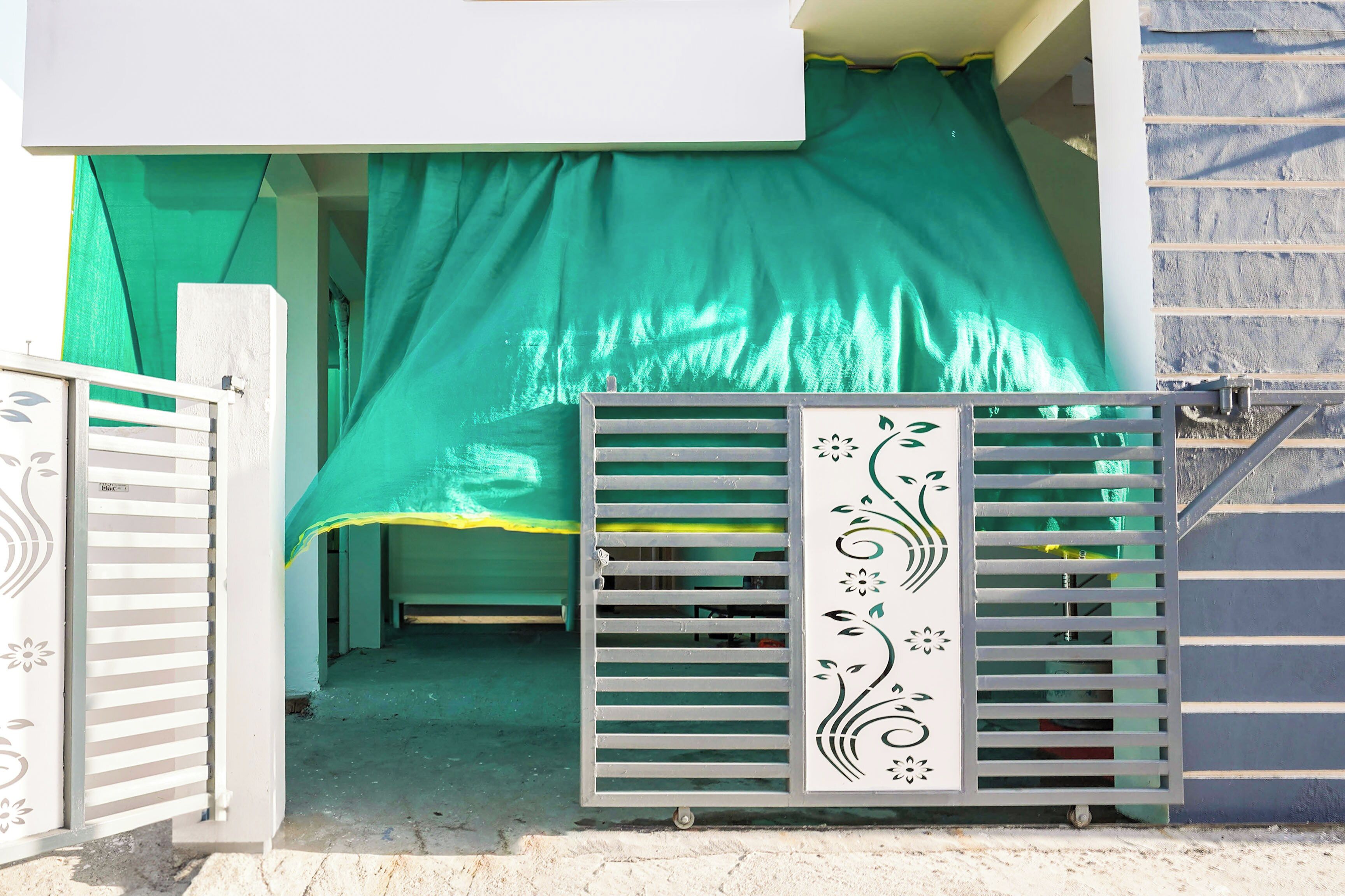 Un cancello di ingresso chiuso da una struttura metallica ornata, con un tessuto verde drappeggiato e un pavimento in cemento che conduce a un edificio.