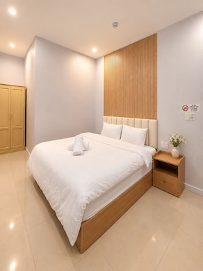 Una habitación de hotel moderna con una cama grande, un cabecero de madera, una mesita de noche y una lámpara de pared.