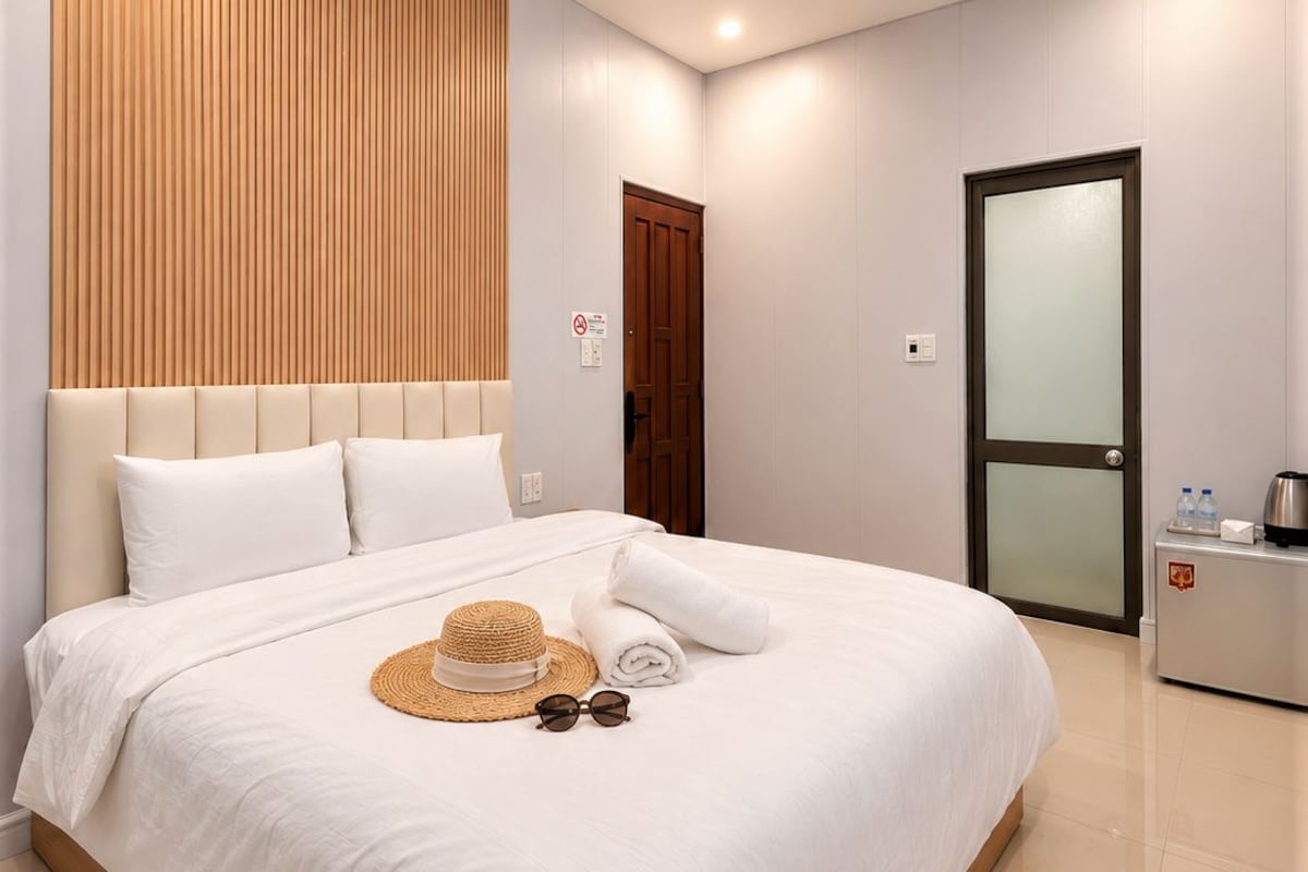 Habitación de hotel moderna con una cama grande, un panel de pared de madera, una puerta con un panel de vidrio esmerilado y una mesita de noche con una tetera.