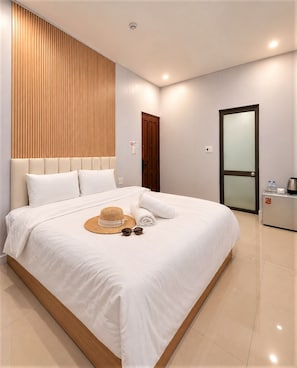 Habitación de hotel moderna con una cama grande, un panel de pared de madera, una puerta con un panel de vidrio esmerilado y una mesita de noche con una tetera.