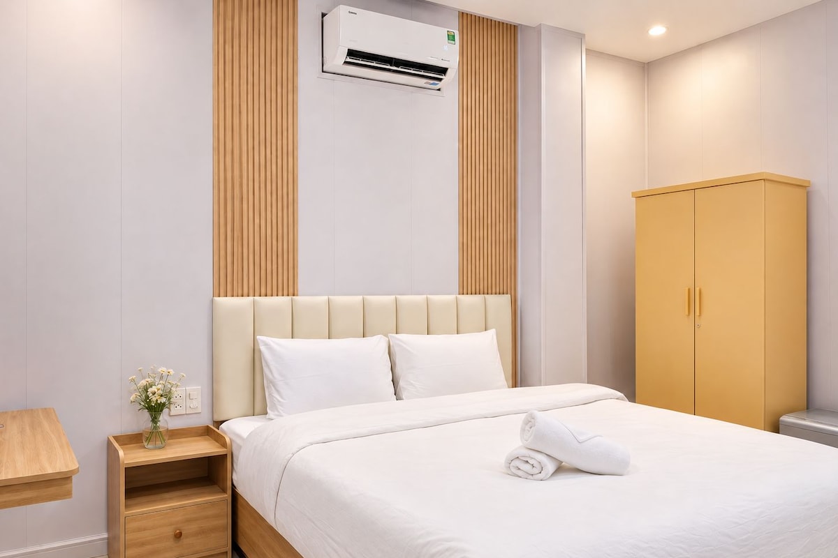 Una habitación de hotel con una cama, una mesita de noche de madera, un armario y un equipo de aire acondicionado.