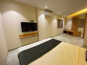 Une chambre d’hôtel comprenant un lit, un téléviseur à écran plat fixé au mur, un banc en bois, une armoire et un appareil de climatisation.