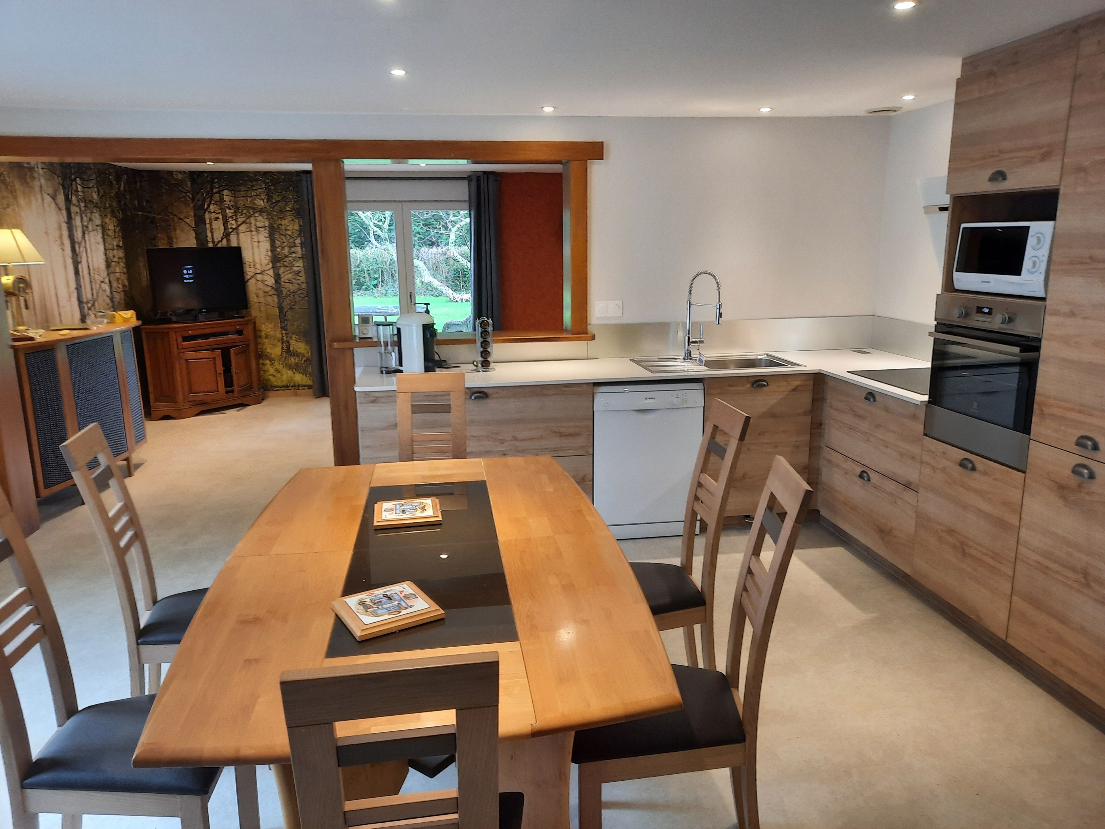 Une cuisine moderne avec un coin repas, des meubles en bois, un lave-vaisselle et un téléviseur.