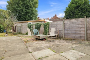 A backyard with a concrete patio, a wooden fence, and a small shed. - Serene 3-bedroom apartment in the heart of Manchester (Manchester)