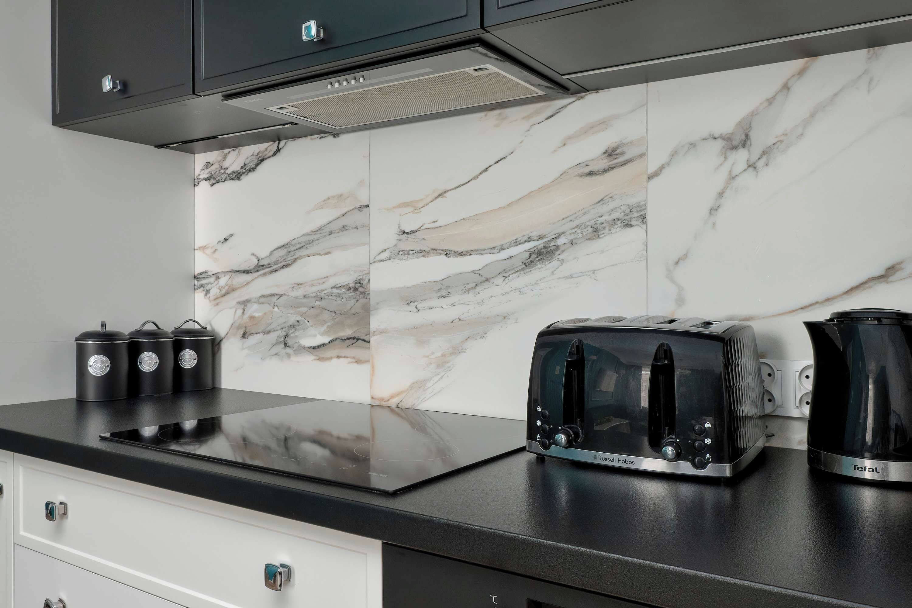 A kitchen with a black countertop, a toaster, a kettle, and a set of black containers.