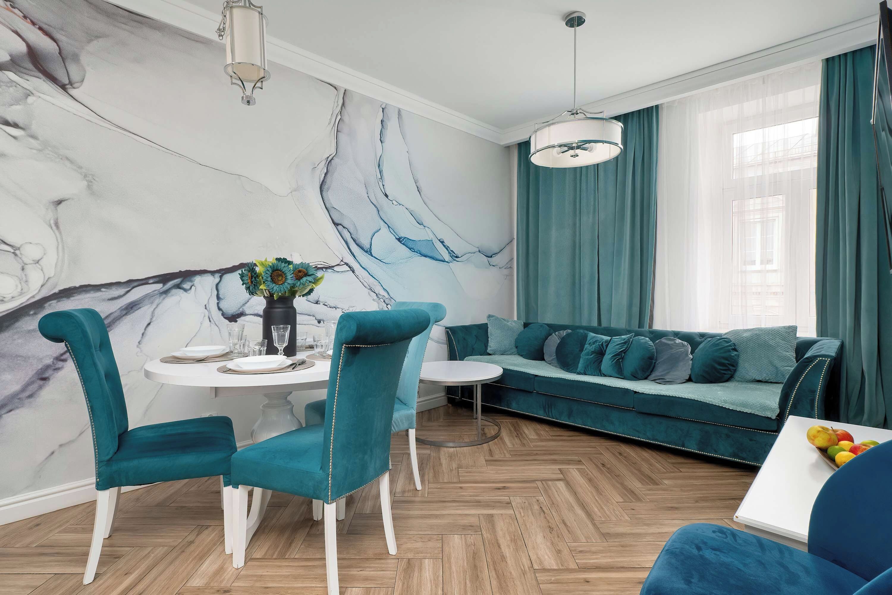 Ein modernes Wohnzimmer mit einer Marmorwand, türkisblauem Mobiliar und einem Essbereich mit weißen Stühlen und einem Tisch für zwei Personen.