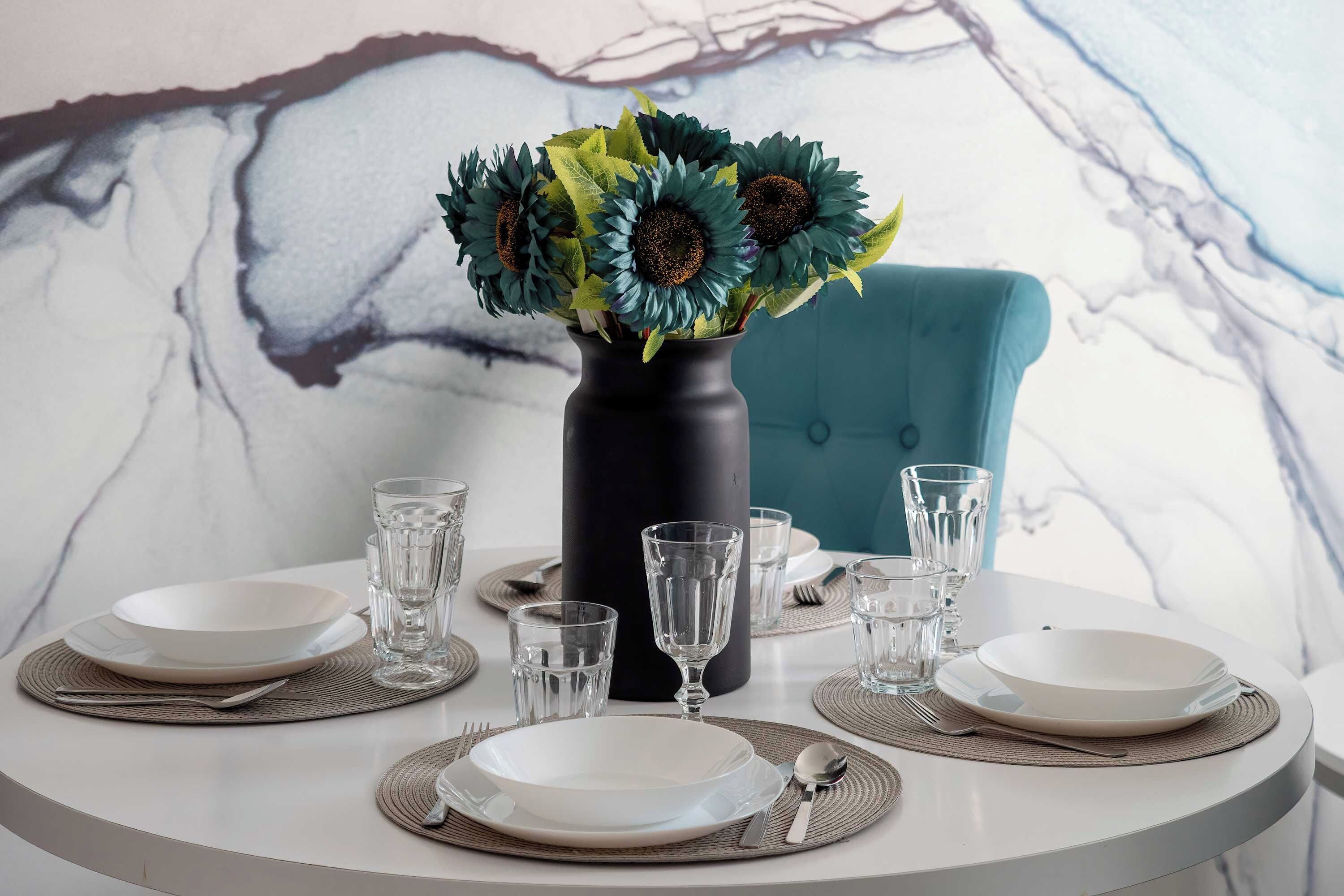 A dining table set with plates, glasses, and a vase with sunflowers.