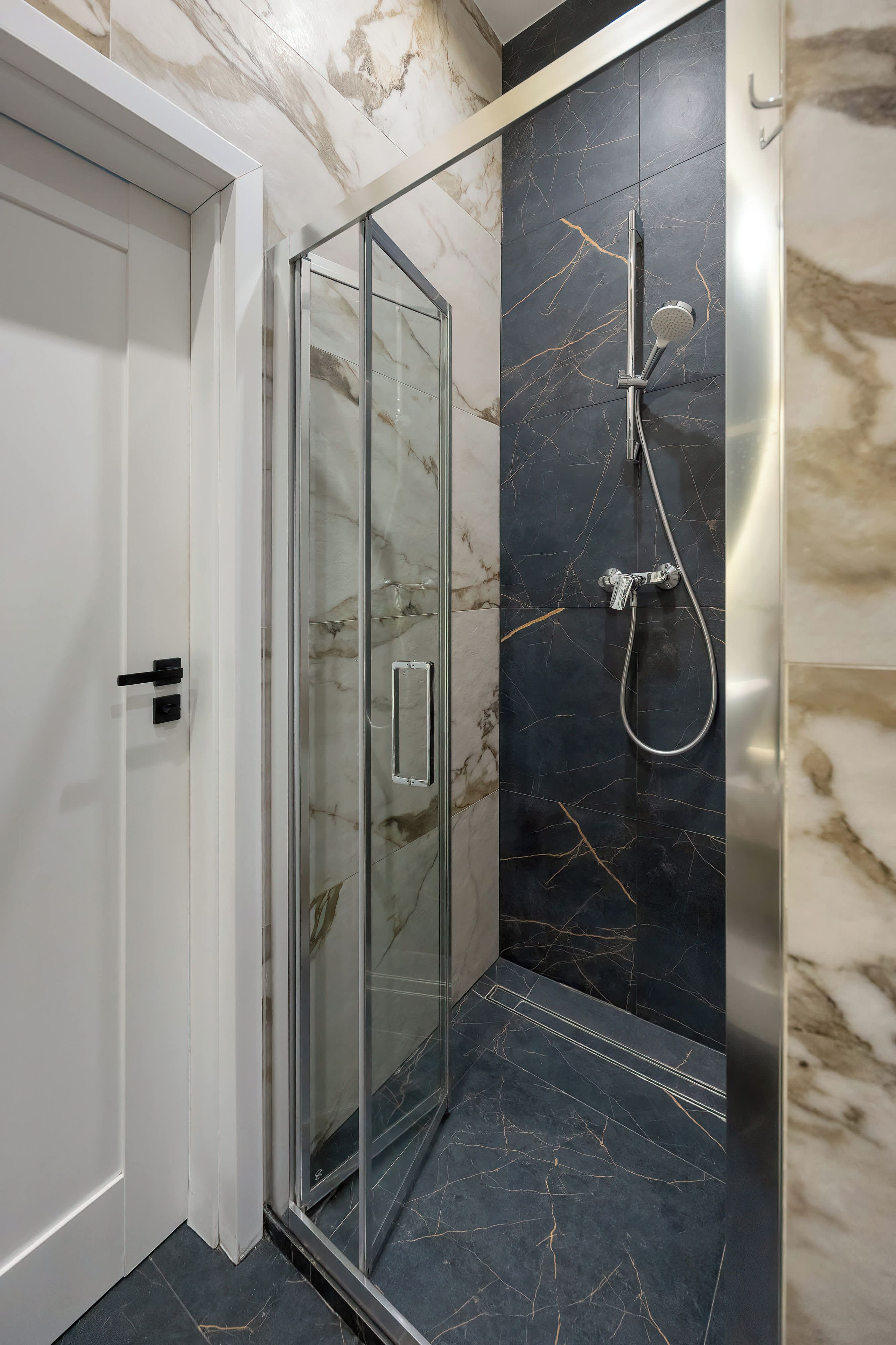 A modern bathroom with a glass shower enclosure, a handheld showerhead, and a wall-mounted faucet.