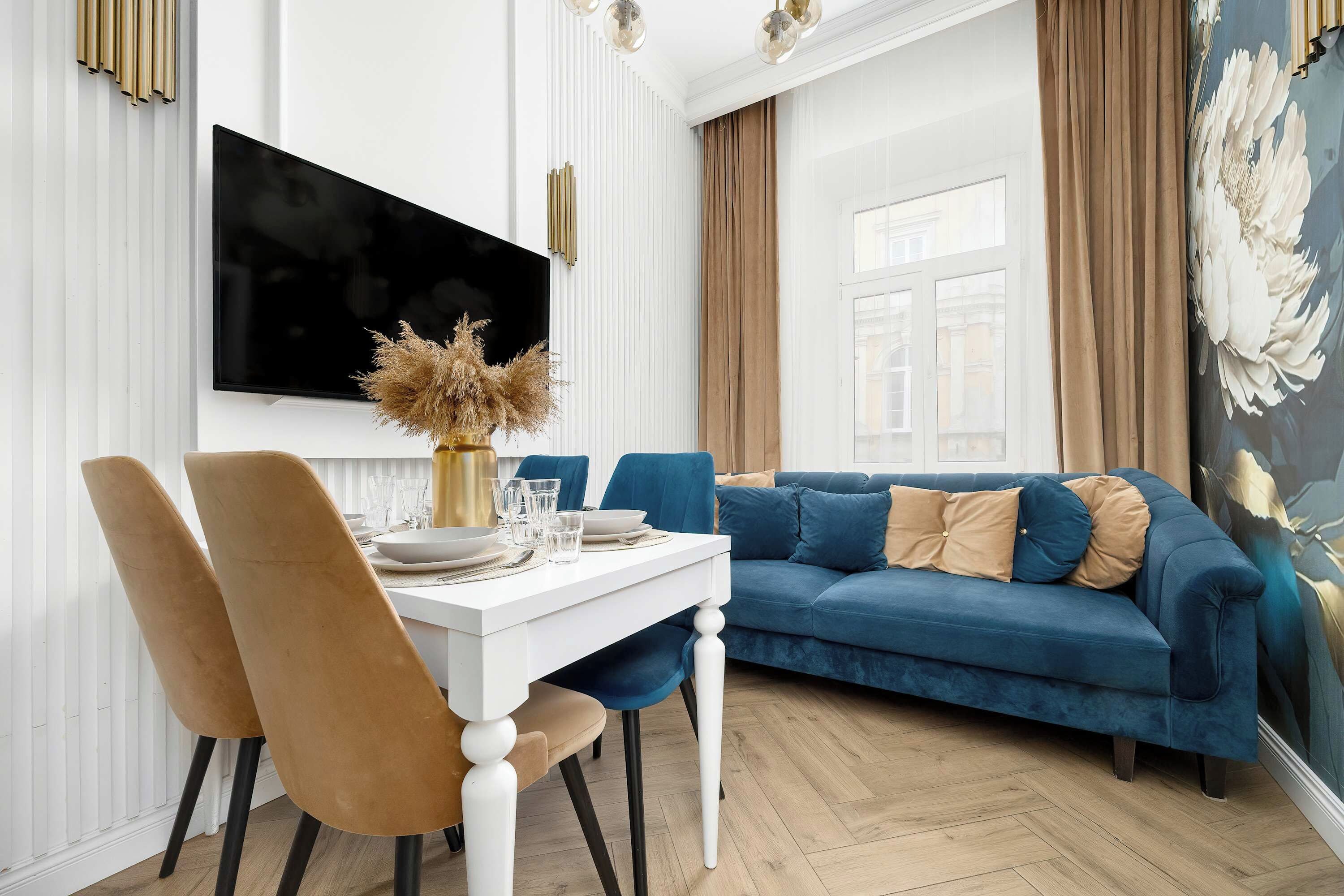 Ein modernes Wohnzimmer mit einem weißen Esstisch, einem blauen Sofa und einem an der Wand befestigten Flachbildfernseher.