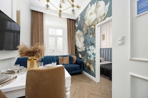 Ett modernt vardagsrum med en blå soffa, ett matbord med glas och bestick samt en stor tapet med blommönster.