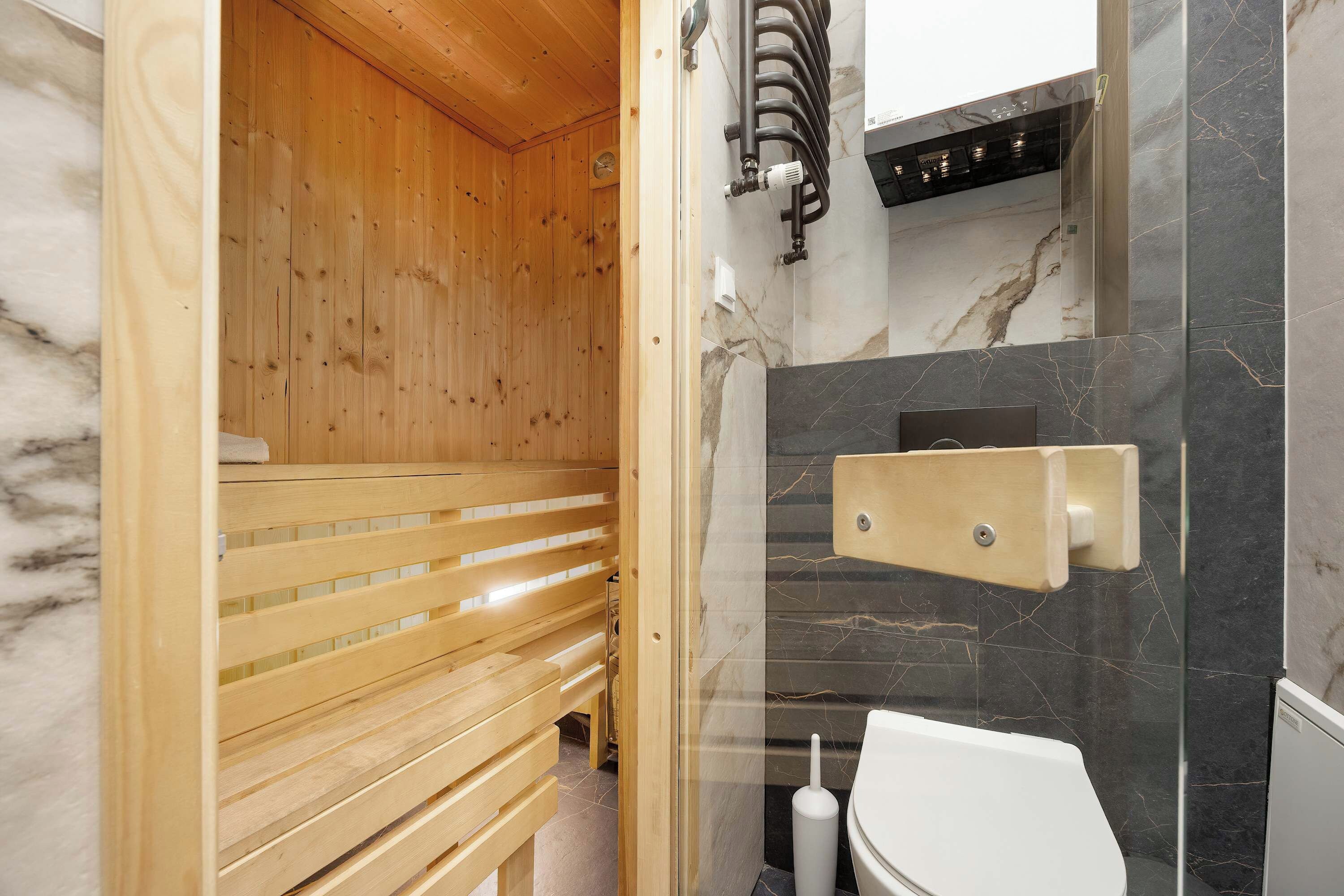 Eine Sauna mit Holzbänken, einer Wand aus Marmorfliesen und einer weißen Toilette.