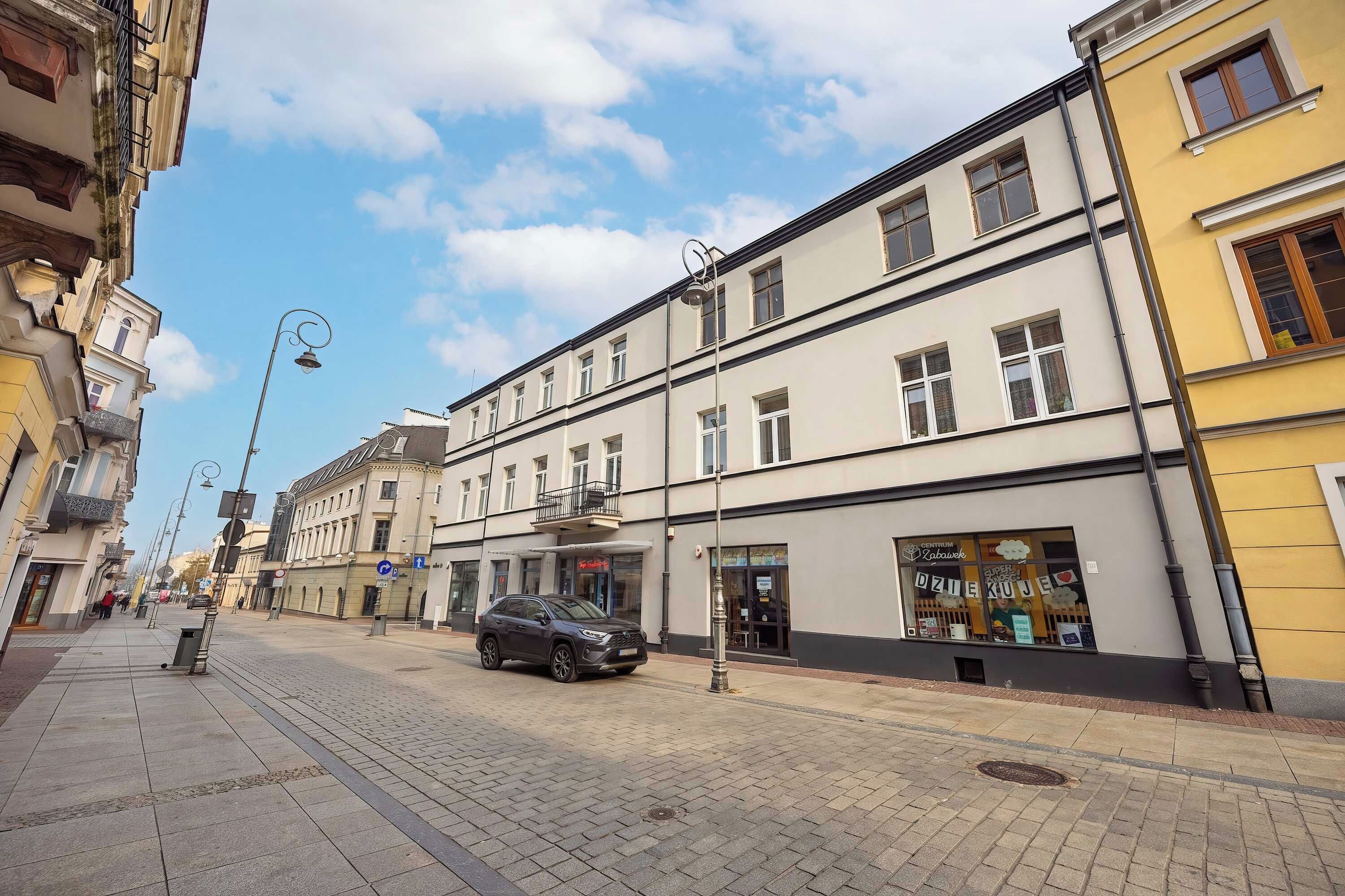 Une vue de rue montrant un immeuble avec une entrée au rez-de-chaussée, un magasin visible avec une enseigne, et une voiture garée.